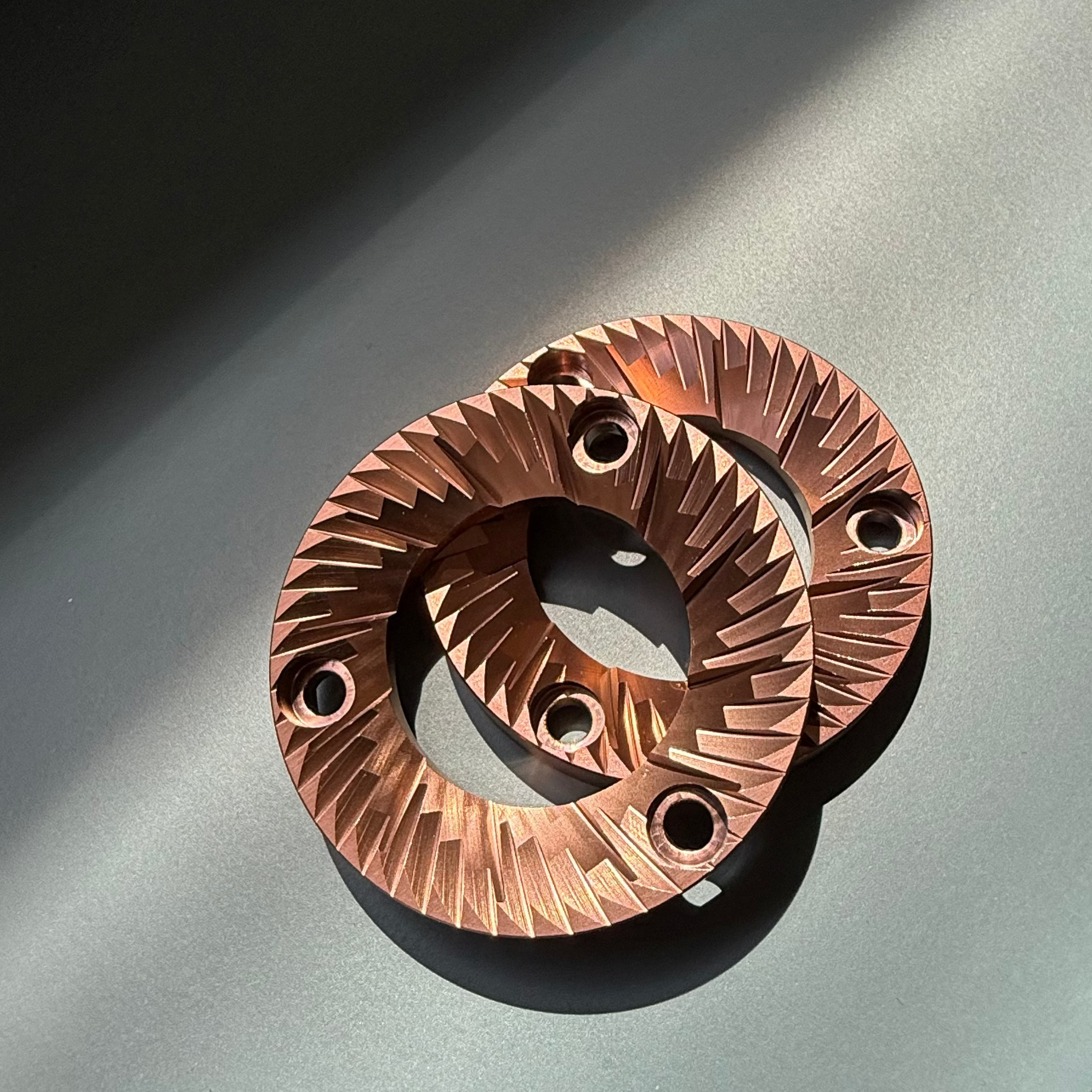 Pair of 54mm Red titanium flat burrs for DF54 Coffee Grinder - against turquoise background