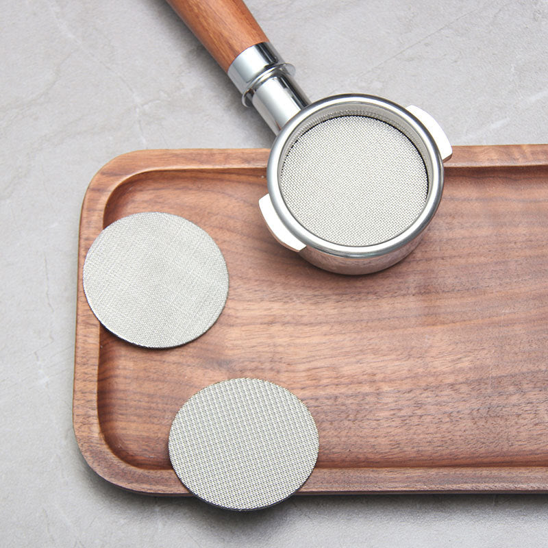 Fine mesh stainless steel espresso puck screens displayed beside a portafilter on a wooden tray - Grind Logic