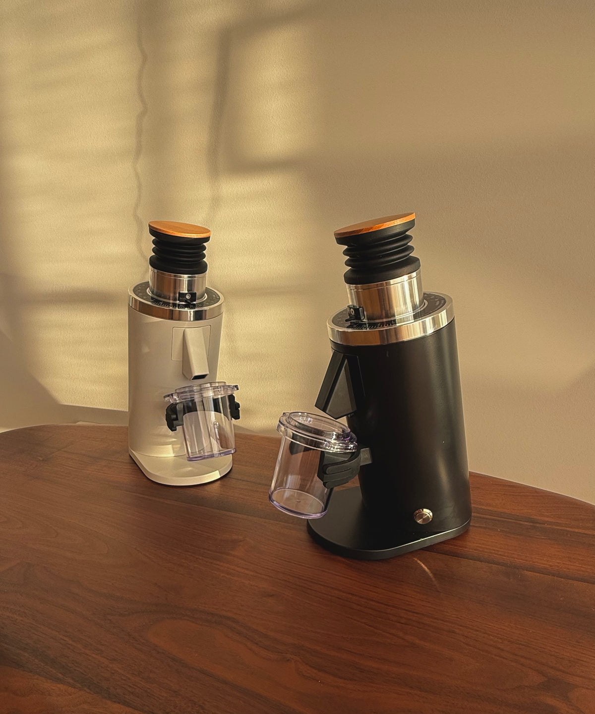 Black and white DF54 single-dose espresso grinders on a wooden bench in warm natural light.