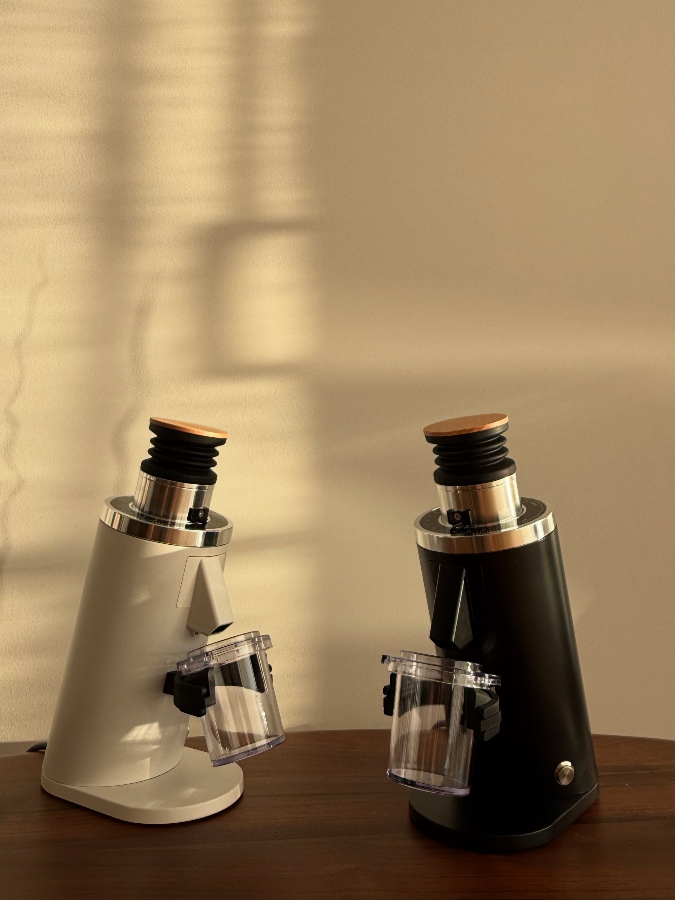 Two DF54 coffee grinders, one white and one black, on a wooden surface with a neutral background.