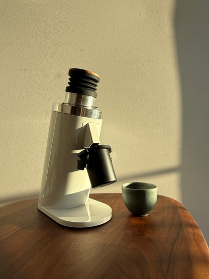 White DF64 Gen 2 Coffee GRinder on a wooden surface with a beige wall background